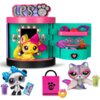 Zestaw figurek LITTLEST PET SHOP Słodka stylowa stacja LPS00722 przedstawia kolorową stację z otwartymi drzwiami, w której znajduje się żółta figurka z różową kokardą. Obok stacji widoczne są dodatkowe akcesoria, w tym różowe pudełko z logo "LPS", fioleto
