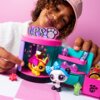 Zestaw figurek LITTLEST PET SHOP Słodka stylowa stacja LPS00722 przedstawia kolorową scenkę z dwoma figurkami zwierzątek, z których jedno jest żółte z różową kokardą, a drugie biało-czarne z niebieską kokardą. Na górze zestawu widnieje napis "LPS" z symbo