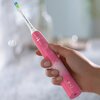 Różowa szczoteczka soniczna marki Philips Sonicare jest trzymana w dłoni, z widocznym przyciskiem zasilania na uchwycie. Na główce szczoteczki znajduje się napis "PHILIPS SONICARE".