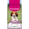 Opakowanie karmy dla psa z widocznym logo "EUKANUBA" na różowym tle, poniżej zdjęcie szczeniaka na tle zielonej trawy z kwiatami. Na dole opakowania znajduje się napis "PUPPY 1-12 MONTHS" oraz informacje o składnikach i wadze "12 kg".
