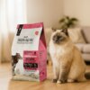 Na zdjęciu znajduje się opakowanie karmy dla kota "WIEJSKA ZAGRODA Monobiałkowa Wołowina 3 kg" z widocznym tekstem: "KOT DOROSŁY ADULT CAT MONOPROTEINOWA WOŁOWINA", a obok siedzi kot na drewnianej podłodze w domowym wnętrzu. Opakowanie ma różowo-białą kol