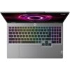 Laptop z podświetlaną klawiaturą w kolorach tęczy, z widocznym logo "Lenovo" na obudowie. Na ekranie wyświetlany jest abstrakcyjny, fioletowy wzór.