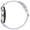 Srebrny smartwatch z fioletowym paskiem, widoczny z boku, z okrągłym przyciskiem i zapięciem. Na boku koperty widoczna jest liczba "15".