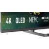 Fragment ekranu telewizora z widocznymi napisami: "4K | QLED | MEMC" oraz logo "Dolby ATMOS". Tło jest w odcieniach zieleni z delikatnym wzorem, a w rogu ekranu widoczny jest fragment żółtego samochodu wyścigowego.