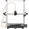 Na zdjęciu znajduje się drukarka 3D z widocznym napisem "ANYCUBIC KOBRA 3 MAX" na ramie oraz panelem sterowania z wyświetlaczem. Drukarka ma metalową konstrukcję i pomarańczowy przewód prowadzący do głowicy drukującej.