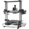 Na zdjęciu znajduje się drukarka 3D z metalową ramą i ruchomym stołem roboczym. Urządzenie ma widoczne elementy mechaniczne, takie jak prowadnice i silniki, oraz dyszę do druku.