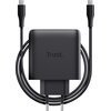 Czarny zasilacz do laptopa z logo "Trust." na środku, z dołączonym kablem USB-C owiniętym wokół urządzenia. Produkt ma kompaktowy, prostokątny kształt z widocznymi dwoma bolcami wtyczki.