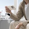 Na zdjęciu widać osobę trzymającą smartfon, który jest podłączony do białego powerbanku z wyświetlaczem pokazującym "99%" oraz oznaczeniem "45W". W tle znajduje się srebrna walizka.