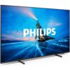 Telewizor z wyświetlaczem pokazującym krajobraz z osobą stojącą na skale nad zamarzniętym jeziorem, z napisem "PHILIPS" na środku ekranu. Obudowa telewizora jest cienka, a ekran wsparty jest na dwóch prostych nóżkach.