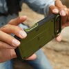 Na zdjęciu widoczne jest zielone etui SUPCASE Ub Pro na telefon, trzymane w dłoniach. Etui ma solidną konstrukcję z wyraźnymi elementami ochronnymi i otworem na aparat.