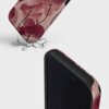 Etui na telefon z motywem różowych kwiatów i napisem "BURGA" leży na powierzchni z pęknięciami. Produkt ma ciemne, ochronne krawędzie.