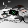 Na zdjęciu znajduje się telefon w etui umieszczony na stojaku, z widocznym ekranem pokazującym ikonę ładowania i napis "87% Charged". Wokół rozmieszczone są różne akcesoria, w tym uchwyty i ładowarki, a na jednym z nich widnieje logo "Ringke".