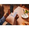 Na zdjęciu widać osobę trzymającą telefon z wyświetlonymi opcjami menu oraz biało-jasnoniebieski dysk SSD podłączony do telefonu za pomocą kabla. Na stole znajduje się szklanka z napojem, plasterkiem cytryny i miętą oraz talerz z pieczywem.
