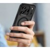 Na zdjęciu widoczne jest czarne, matowe etui na telefon z trzema dużymi otworami na aparaty oraz okrągłym wzorem na środku. Etui jest trzymane w dłoni na tle rozmytego wnętrza.