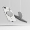Przezroczyste etui na telefon z widocznym okrągłym elementem magnetycznym MagSafe, zawieszone na białym przewodzie, na jasnym tle. Obok etui znajduje się drugi, rozmyty element magnetyczny, również zawieszony na przewodzie.