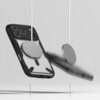 Przezroczysto-czarne etui na telefon z widocznym okrągłym elementem magnetycznym, zawieszone na białym przewodzie, obok znajduje się drugi podobny element. Tło jest jednolite, jasnoszare.