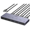 Na zdjęciu znajduje się przełącznik KVM z logo "UGREEN" na górze, z trzema przyciskami i kilkoma portami USB oznaczonymi jako "5Gbps". Widoczne są również podłączone kable HDMI i USB-C, a w prawym dolnym rogu znajduje się napis "8K 60Hz".