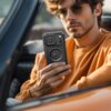 Mężczyzna w okularach przeciwsłonecznych trzyma w ręku czarne etui na telefon z widocznymi detalami konstrukcyjnymi. Etui ma wyraźne elementy ochronne i okrągły wzór na środku.