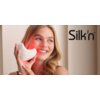 Na zdjęciu widoczna jest osoba trzymająca urządzenie emitujące czerwone światło, z logo "Silk'n" umieszczonym w prawym górnym rogu. Produkt ma opływowy kształt i jest koloru białego.