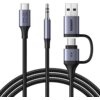 Na zdjęciu widoczny jest pleciony kabel z trzema różnymi złączami: USB, USB-C oraz mini jack. Na złączach znajdują się oznaczenia: "UGREEN", symbol "IN" oraz ikony przedstawiające wejścia i wyjścia.