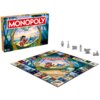 Pudełko gry planszowej "Monopoly Lilo & Stitch" z kolorową grafiką przedstawiającą postacie z filmu, obok rozłożona plansza z identycznym motywem oraz sześć metalowych pionków. Na pudełku widnieje napis "Monopoly Lilo & Stitch", a na planszy znajduje się 