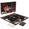 Pudełko gry planszowej "Cluedo Stranger Things" z widocznymi postaciami i potworem z serialu, obok rozłożona plansza z różnymi lokacjami oraz karty postaci. Na pudełku widnieje logo "Stranger Things" i napis "Cluedo", a na planszy centralnie umieszczony j