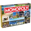 Pudełko gry planszowej z napisem "MONOPOLY" na czerwonym tle oraz "KASZËBË" na dole, ozdobione zdjęciami przedstawiającymi krajobrazy, zabytki i ludzi w tradycyjnych strojach. W lewym górnym rogu widnieje napis "Od zera do milionera", a w dolnym lewym rog
