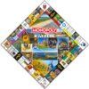 Plansza gry Monopoly Kaszuby z centralnym napisem "MONOPOLY KASZËBË" otoczona jest zdjęciami i grafikami związanymi z regionem Kaszub, w tym krajobrazami, budynkami i elementami kultury. Na polach planszy widoczne są różne ilustracje oraz napisy, takie ja