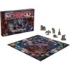 Pudełko gry planszowej "Monopoly Wiedźmin" z widocznymi postaciami z serii oraz plansza do gry z centralnym logo "Monopoly Wiedźmin". Obok planszy znajdują się metalowe pionki w kształcie zamku, smoka, lutni, hełmu i konia.