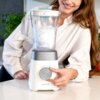 Blender kielichowy w kolorze białym z przezroczystym pojemnikiem wypełnionym lodem, z widocznym logo "cecotec" na podstawie. Osoba w białej koszuli obsługuje blender, trzymając pokrętło regulacji.