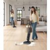Na zdjęciu widać osobę używającą odkurzacza TINECO Floor One I6 Stretch Plus do sprzątania rozlanego płynu na drewnianej podłodze w nowoczesnym, jasnym wnętrzu kuchni. W tle znajdują się białe szafki kuchenne, wyspa z hokerami oraz wiszące lampy.