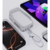 Na zdjęciu znajduje się biały powerbank z napisem "AUKEY" oraz "10000" na obudowie, z wyświetlaczem pokazującym informacje o ładowaniu. Obok powerbanku widoczne są trzy urządzenia elektroniczne z wyświetlaczami, a do powerbanku podłączony jest biały przew