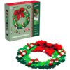Pudełko z klockami plastikowymi przedstawia kolorowy wieniec świąteczny z napisem "CHRISTMAS WREATH" oraz informacjami: "500 PIECES", "6 COLORS", "PUZZLE MAT", "PUZZLE IN 2D", "CREATE IN 3D". Obok pudełka znajduje się złożony wieniec z klocków w kolorach 