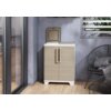 Kremowo-beżowy stojak na worki KETER Split Premium Wood 2x110L stoi na drewnianej podłodze przy szarej ścianie, z otwartą pokrywą na górze. Obok znajduje się metalowe krzesło z poduszką, a w tle widać przeszklone drzwi i okno z roślinnością.
