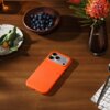 Na drewnianym stole leży pomarańczowe etui na telefon z widocznym napisem "beats", obok którego znajdują się miska z jagodami, talerz z warzywami oraz wazon z kwiatem. W tle widoczny jest fragment serwetki i łyżeczka.