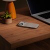 Na drewnianym biurku znajduje się etui na telefon w kolorze alpejskiej szarości, obok laptopa i małej doniczki z sukulentem. Na etui widoczny jest napis "beast".