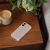 Na drewnianym stoliku znajduje się beżowe etui na telefon z widocznymi dwoma otworami na aparaty oraz napisem "mochi" na dole. Obok etui stoi filiżanka z kawą oraz doniczka z zieloną rośliną.