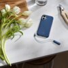 Na zdjęciu znajduje się niebieskie etui na telefon z napisem "beats" na białym blacie, obok białych tulipanów i nożyczek ogrodniczych. W tle widoczna jest szklanka z wodą.