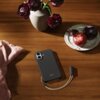 Na drewnianym stole leży granitowo-szare etui na telefon z napisem "beats", obok którego znajduje się talerz z owocami oraz wazon z ciemnoczerwonymi kwiatami. Na stole widoczna jest także różowa tkanina.