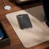 Na zdjęciu widoczne jest granitowo-szare etui na telefon z napisem "beats", leżące na jasnej podkładce na drewnianym biurku. Obok znajduje się okrągła ładowarka bezprzewodowa oraz fragmenty innych przedmiotów, takich jak książki i urządzenia elektroniczne