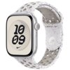 Na zdjęciu widoczny jest szary pasek do zegarka z perforacjami, z logo Nike i Apple Watch na wewnętrznej stronie. Tarcza zegarka wyświetla godzinę 10:09 na tle geometrycznego wzoru.