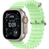 Smartwatch z okrągłym wyświetlaczem pokazuje godzinę 10:09 oraz informacje takie jak "WEST MARINA 385FT - 1M AGO" i "1.8 FT", z neonowo zielonym paskiem o falistej strukturze. Obudowa zegarka jest metaliczna, a przycisk boczny ma pomarańczowy akcent.