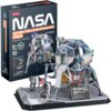 Pudełko z puzzlami 3D przedstawia moduł księżycowy Apollo 11 z napisem "NASA Apollo 11 [Lunar Module] Eagle 3D Puzzle" oraz informacjami: "8+ Age", "93 Pieces", "No Gluing", "No Tools". Obok pudełka znajduje się złożony model modułu księżycowego z flagą U