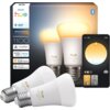 Na zdjęciu znajduje się opakowanie dwóch inteligentnych żarówek LED marki Philips Hue z oznaczeniem "White ambiance 1100", a obok widoczna jest aplikacja na smartfonie z interfejsem do regulacji oświetlenia. Na opakowaniu znajdują się logotypy: "PHILIPS h