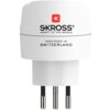 Biały adapter podróżny z trzema metalowymi bolcami, na którym widnieje logo "SKROSS" oraz napisy "ADAPT TO THE WORLD" i "DESIGNED IN SWITZERLAND". Na górze znajduje się czerwony symbol z literą "K".