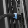 Zbliżenie na tylny panel urządzenia z podłączonym kablem HDMI marki MONTIS, obok widoczne są porty HDMI oraz oznaczenia "DIGITAL AUDIO OUT (OPTICAL)" i "COMMON INTERFACE (CI)". Kabel ma czarną obudowę z niebieskim elementem.