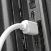 Biały kabel HDMI jest podłączony do portu oznaczonego jako "HDMI 1" na czarnym panelu urządzenia. Obok widoczne są dodatkowe porty HDMI oraz napis "COMMON INTERFACE (CI) HDMI 3".
