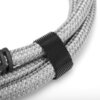 Zbliżenie na szary, pleciony kabel HDMI z czarnym rzepem do organizacji przewodów. Kabel jest zwinięty i widoczny jest fragment plastikowego elementu mocującego.