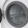 Zdjęcie przedstawia bęben pralki z otwartymi drzwiczkami, ukazujący wnętrze z metaliczną powierzchnią i wzorem w kształcie gwiazdek. Drzwi pralki są częściowo widoczne z zawiasem i uszczelką.