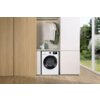 Pralka GORENJE W1NGPI72SBS PL 7kg 1200 obr umieszczona jest w zabudowie, nad nią znajdują się powieszone na wieszakach koszulki oraz kilka butelek z detergentami. Obok pralki widoczny jest fragment ogrodu za dużym oknem.